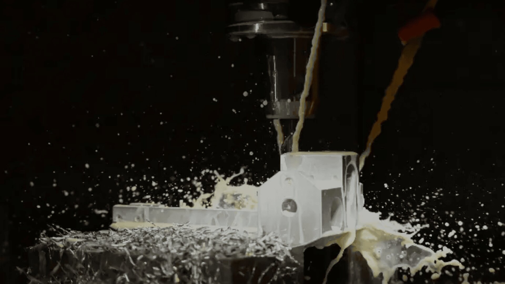 Nahaufnahme einer CNC-Maschine, die Metall schneidet, wobei Kühlflüssigkeit versprüht wird und Metallspäne während der Bearbeitung um das Werkstück herum verstreut werden.