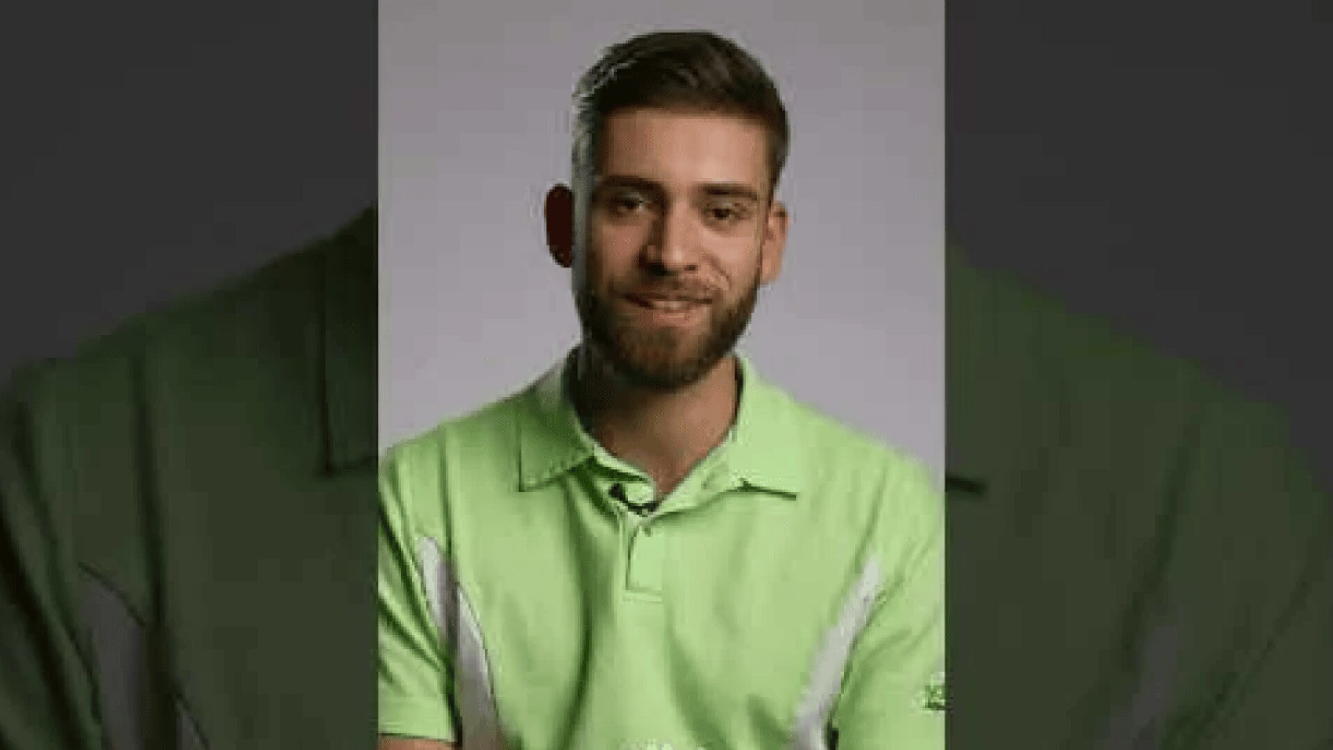 Ein Mann mit kurzen braunen Haaren und einem Bart lächelt leicht. Er trägt ein hellgrünes Hemd mit Kragen und steht vor einem schlichten, neutralen Hintergrund.