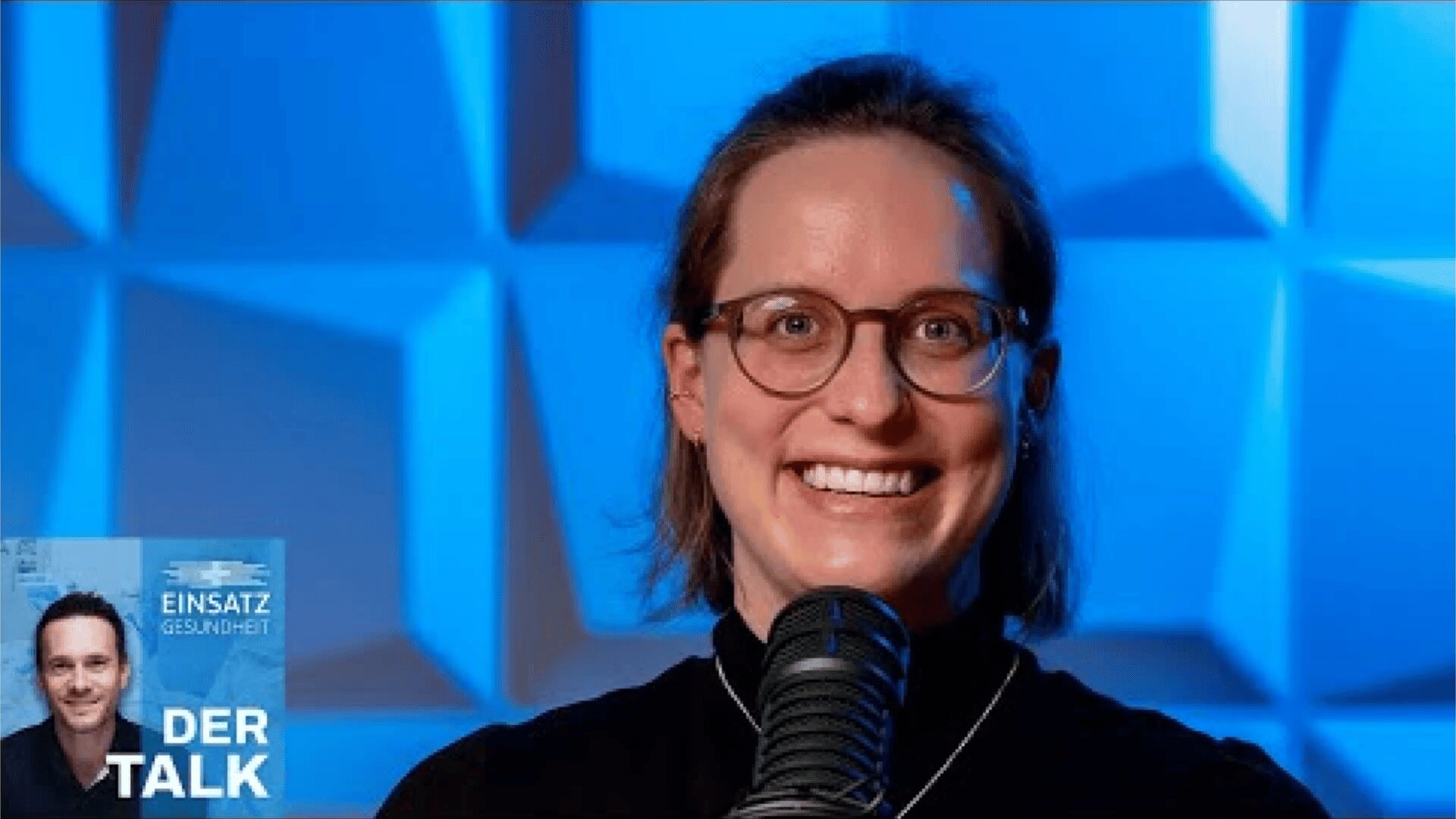 Eine Frau mit Brille und Halskette lächelt vor einem Mikrofon, das vor einem blauen geometrischen Hintergrund steht. In der unteren linken Ecke befindet sich ein Podcast-Logo mit dem Foto eines Mannes und dem Text EINSATZ GESUNDHEIT DER TALK.