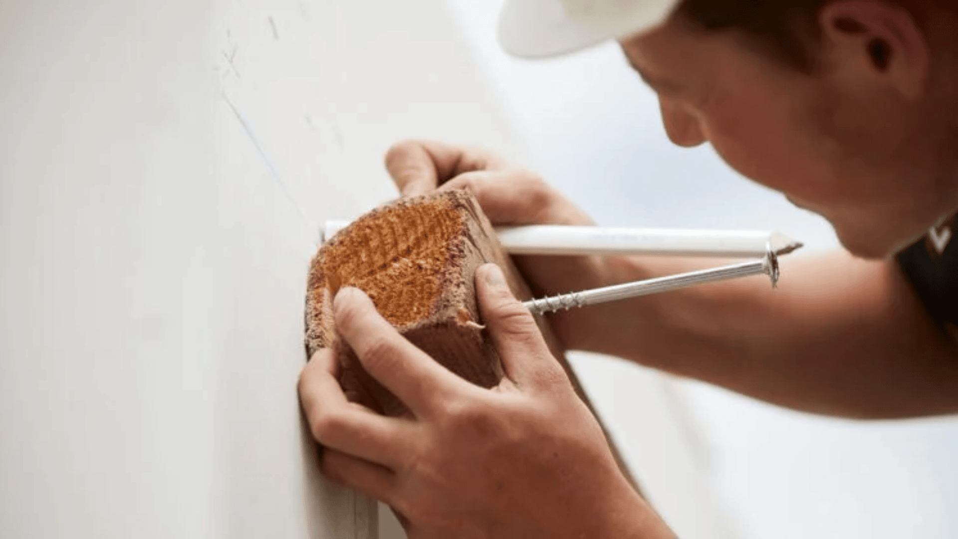 Eine Person hält einen Holzblock an eine Wand und markiert ihn mit einem Bleistift, wobei sie eine große Schraube als Führung verwendet. Sie konzentrieren sich darauf, genaue Messungen für den Bau oder die Installation vorzunehmen.