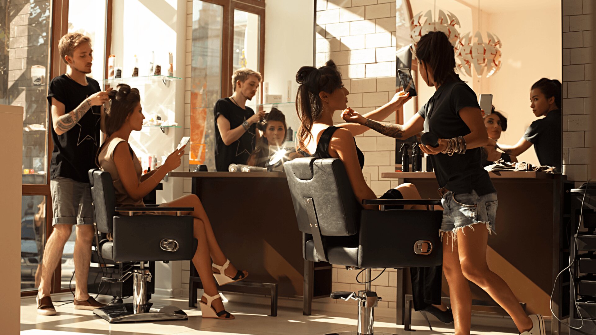 Zwei Friseurinnen arbeiten an Kunden, die auf Stühlen sitzen und deren Haare stylen. Der Salon ist hell mit natürlichem Licht, und andere Mitarbeiter und Kunden sind im Hintergrund zu sehen, was eine lebendige Atmosphäre schafft.