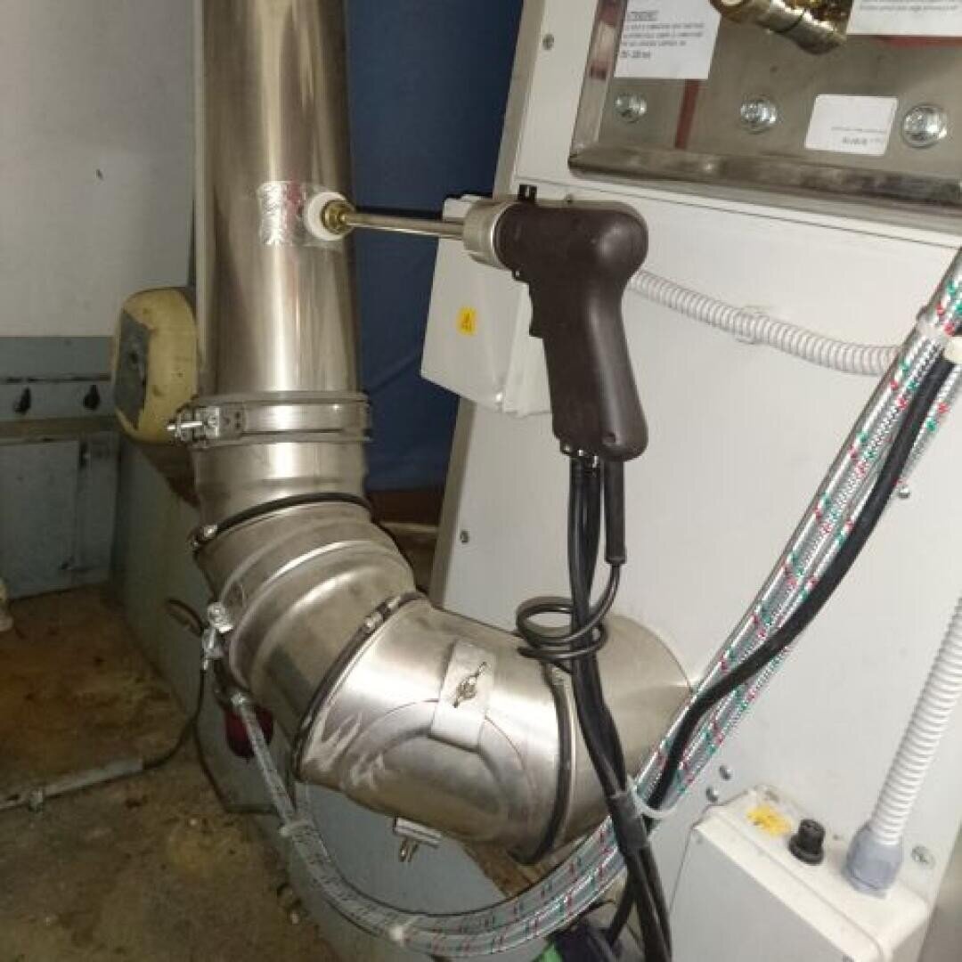 Ein handgehaltenes Ultraschallprüfgerät wird zur Prüfung an einem Metallrohr angebracht. Das Rohr hat mehrere Verbindungen und Biegungen, und das Gerät ist über Kabel mit einem nahe gelegenen Bedienfeld verbunden.