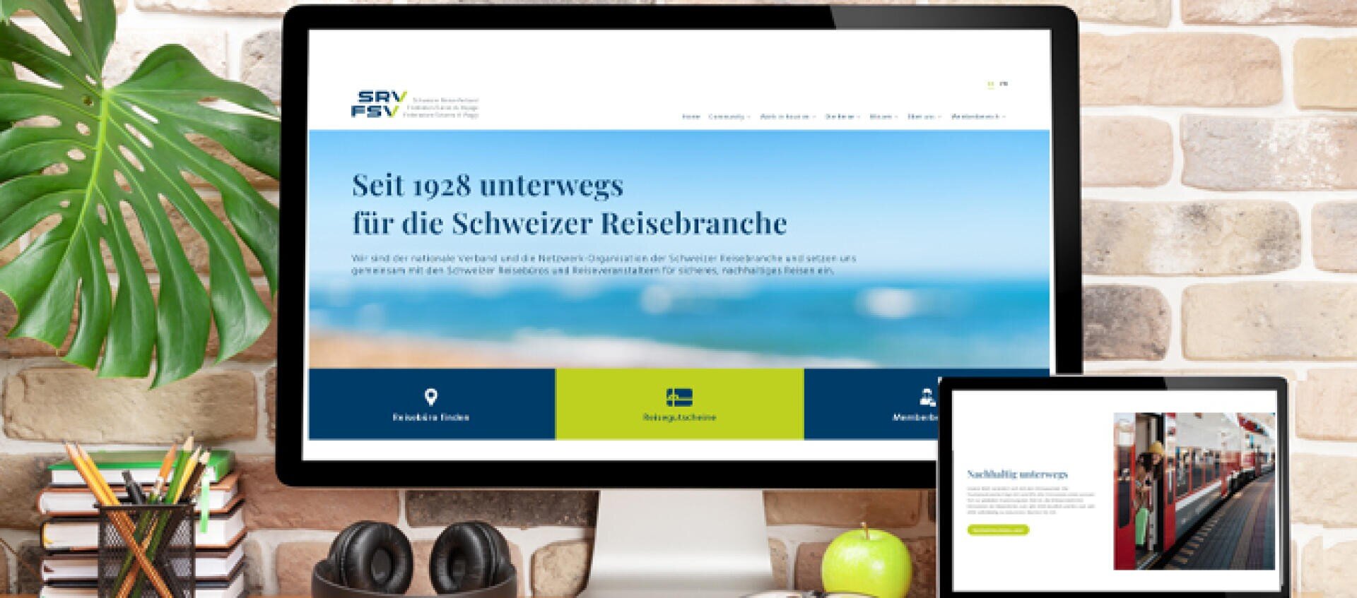 Ein Computer und ein Tablet auf einem Schreibtisch zeigen die Website des Schweizer Reise-Verbandes mit einem Text über seine Arbeit seit 1928. Auf dem Schreibtisch stehen Büromaterialien und eine Grünpflanze, im Hintergrund eine Backsteinmauer.